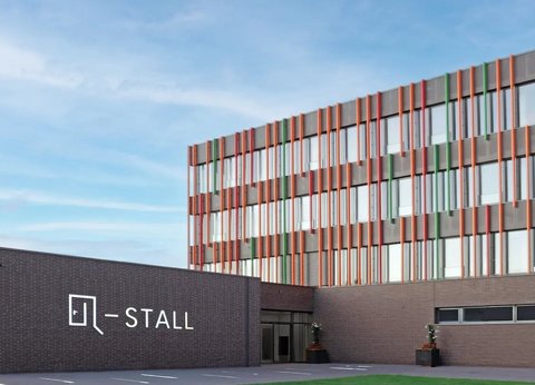 Frontalaufnahme des Q-STALLS, ein moderner Bürokomplex mit Paneelen in Orange, Rot und Grün- den Firmenfarben.